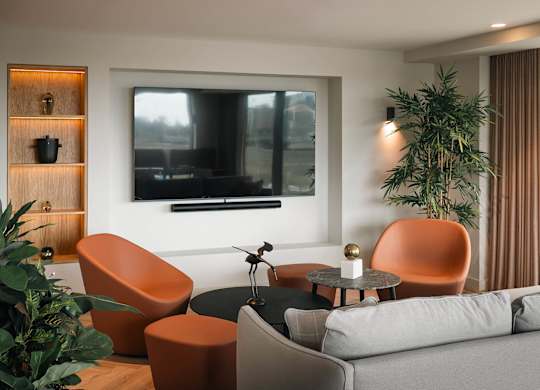 A modern living room with a grey sofa, orange chairs, and a flat screen TV mounted on the wall at Cherrywood Apartments, D18 VY3V, DUBLIN 18