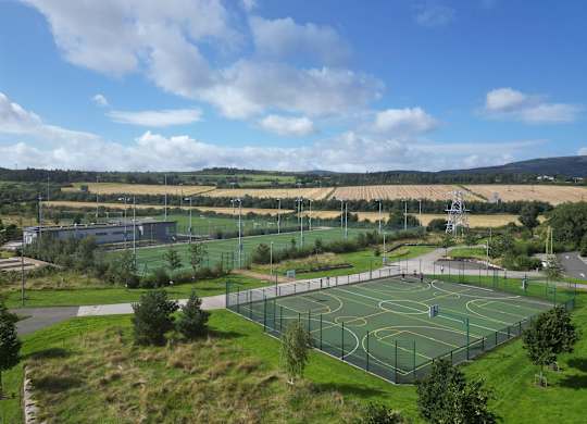 A basketball court surrounded by a green fence with a cloudy blue sky in the background at Cherrywood Apartments, D18 VY3V
