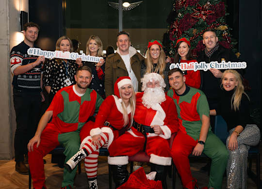 A group of people in Christmas costumes are posing for a photo with Santa and a Christmas tree in the background at Cherrywood Apartments, D18 VY3V, DUBLIN 18