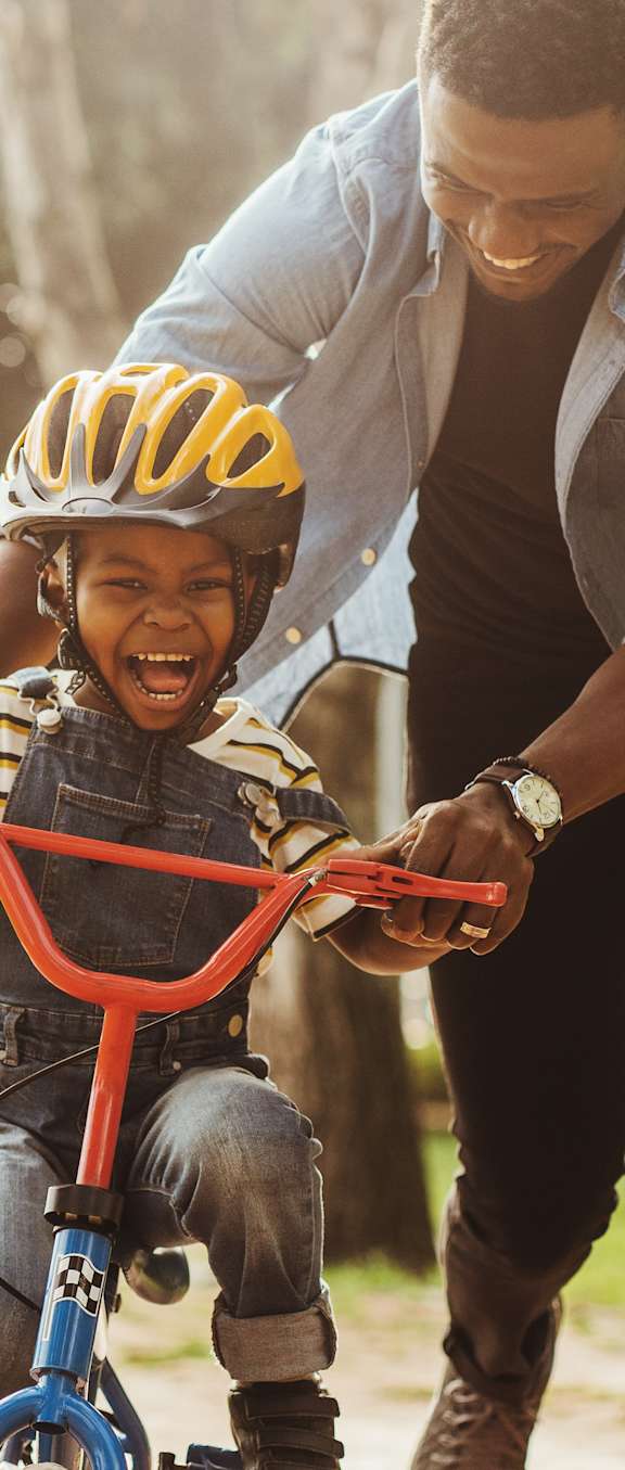 A man is teaching a child to ride a bike in a park.