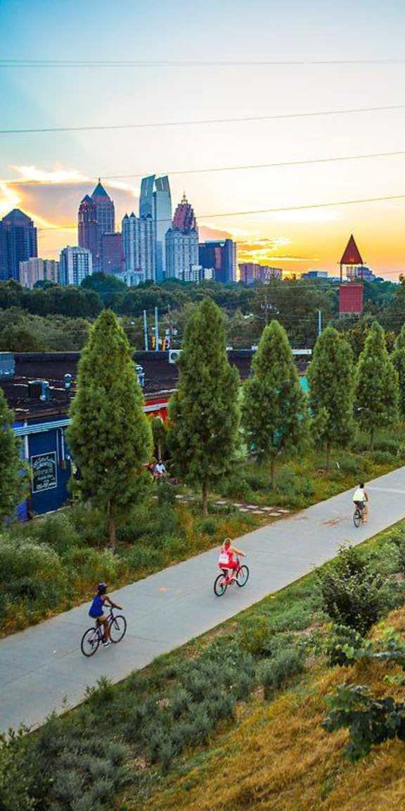 A group of people riding bikes on a path with a city skyline in the background.