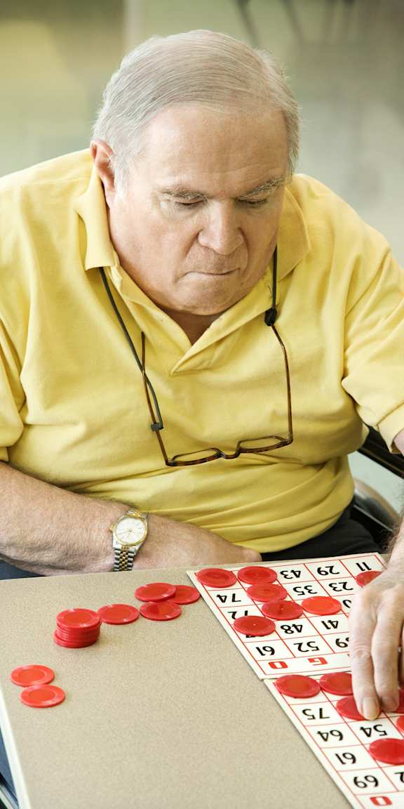 A man in a yellow shirt is playing a game with red pieces on a board.
