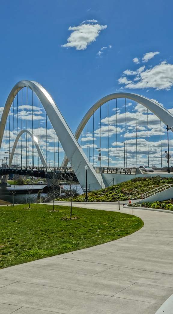 A pedestrian bridge with a curved arch design spans over a body of water.