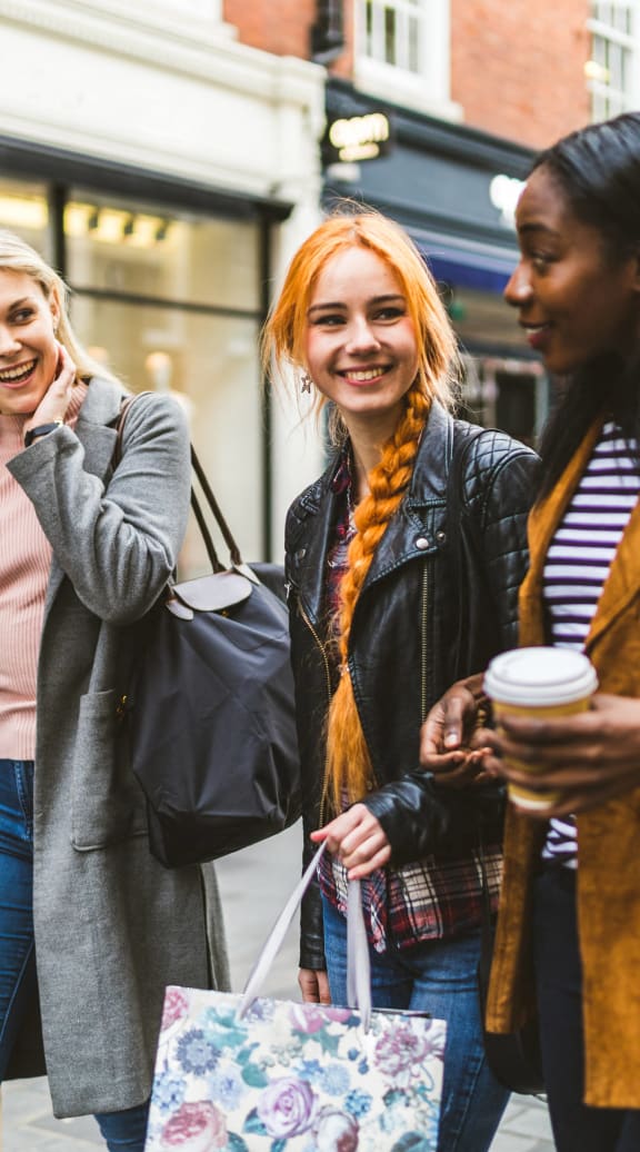 three women walking down the street with shopping bags