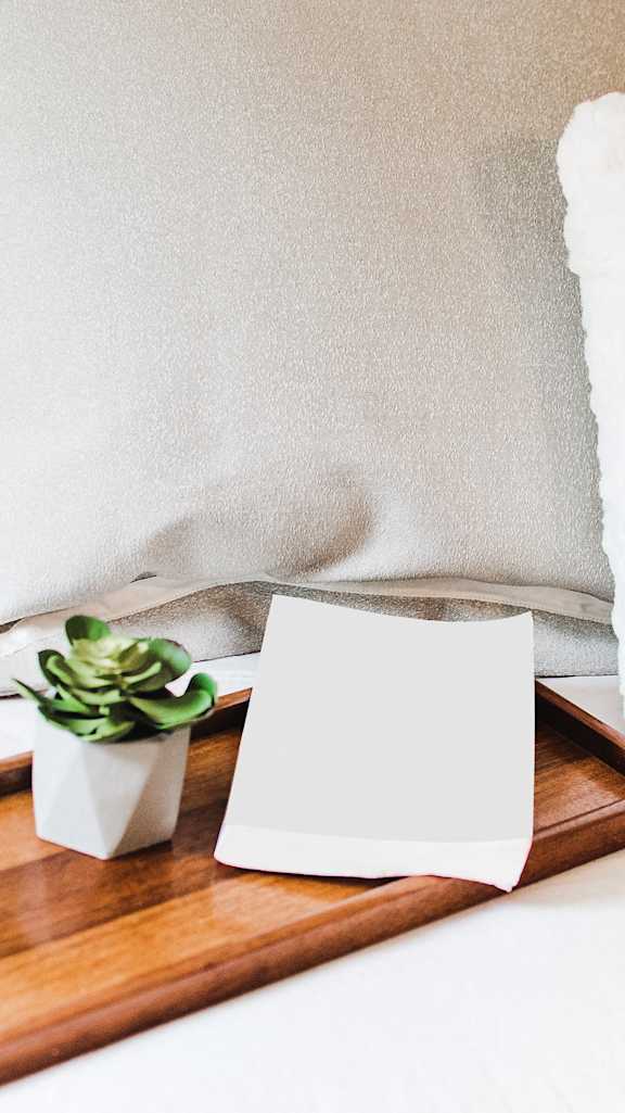 A small succulent plant sits on a wooden tray next to a white card and a white fluffy pillow.