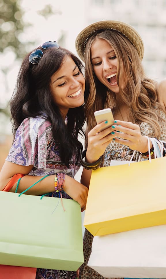 Two women with shopping bags looking at a phone.
