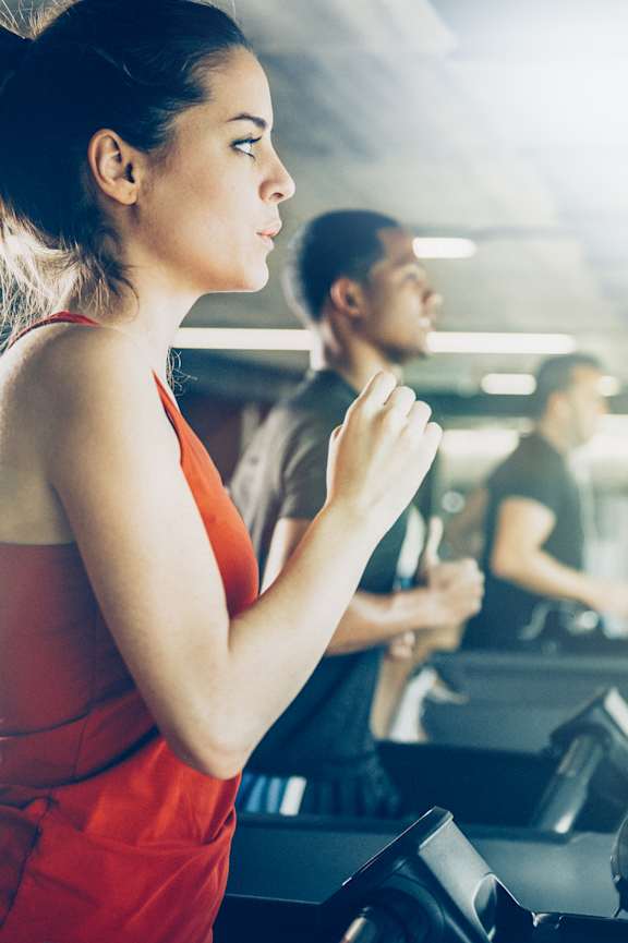 A woman in a red top is running on a treadmill in a gym.