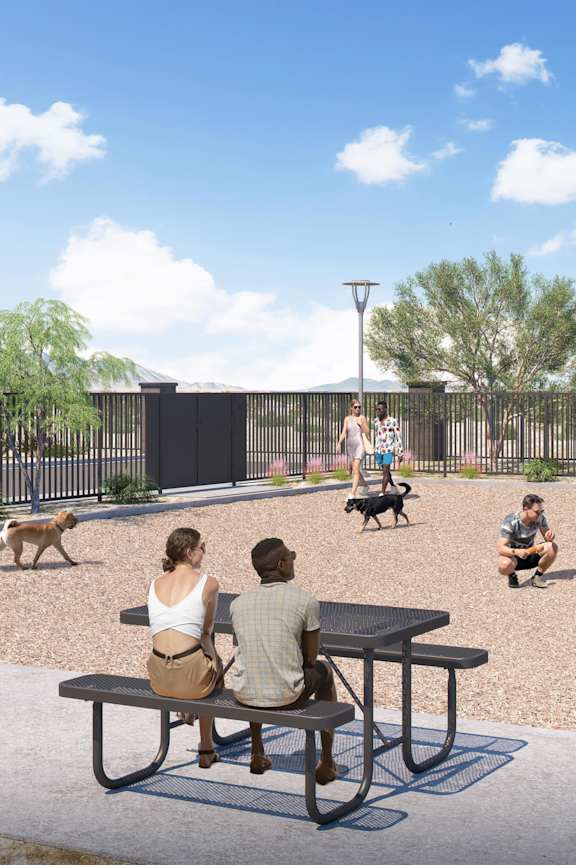 A group of people are sitting at a picnic table with their dogs in a park.