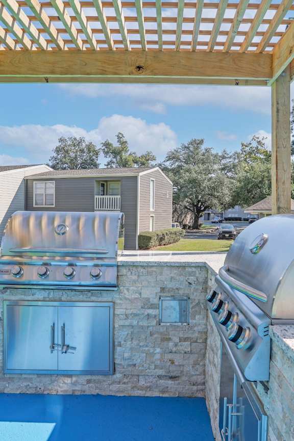 A barbecue grill is in the middle of a patio with a pergola above it.