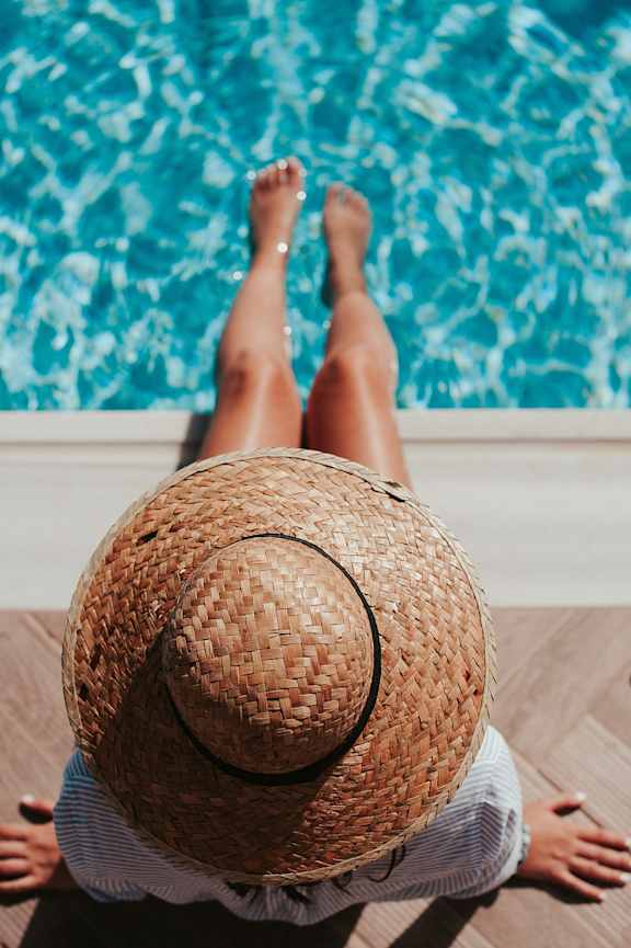 A person wearing a straw hat is sitting by a pool.