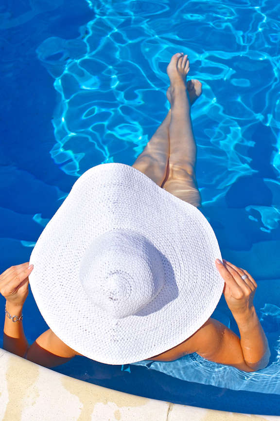 A woman in a white hat is floating in a pool.