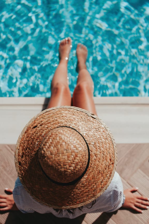 a woman with a straw hat laying on a table in front of a swimming pool