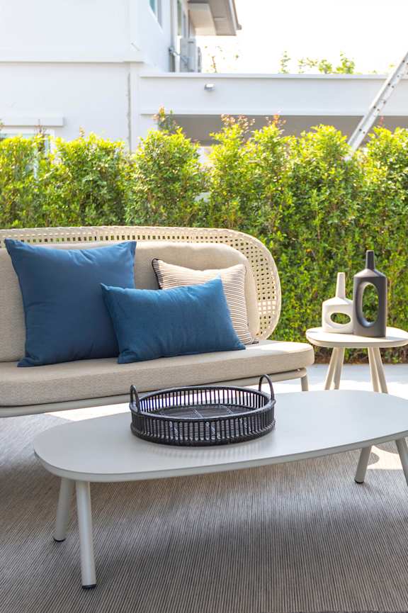 A white wicker sofa with blue pillows and a white coffee table with a basket on it
