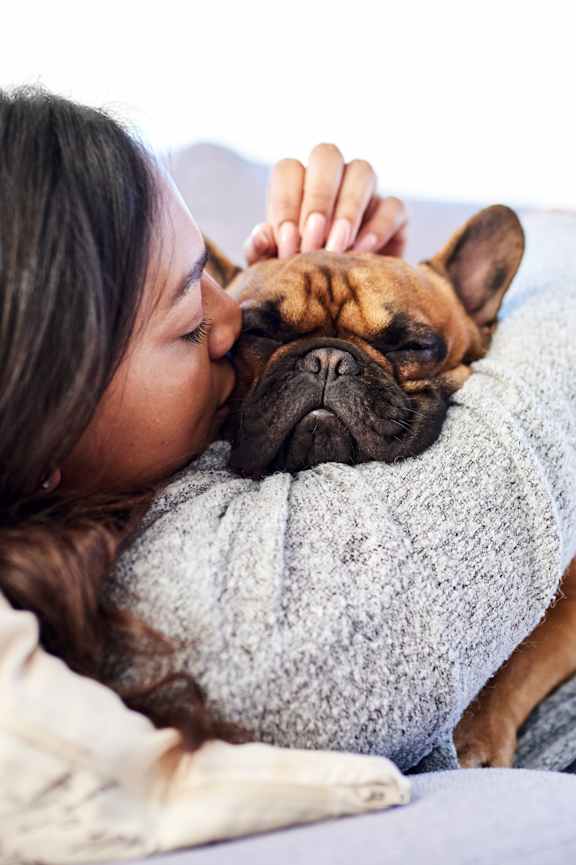 A woman is cuddling with a dog on a grey couch.