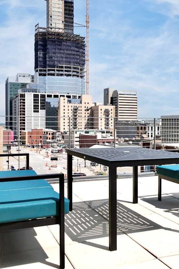 A table and two chairs are on a patio with a city skyline in the background.