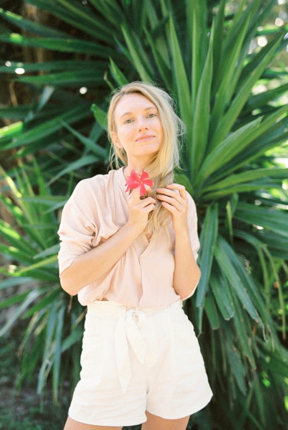 a woman holding a red flower in front of a green plant