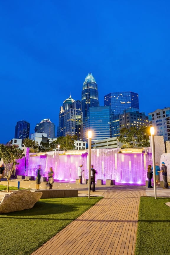 a water fountain in front of a city skyline at night  at Link Apartments® Mint Street, Charlotte, North Carolina