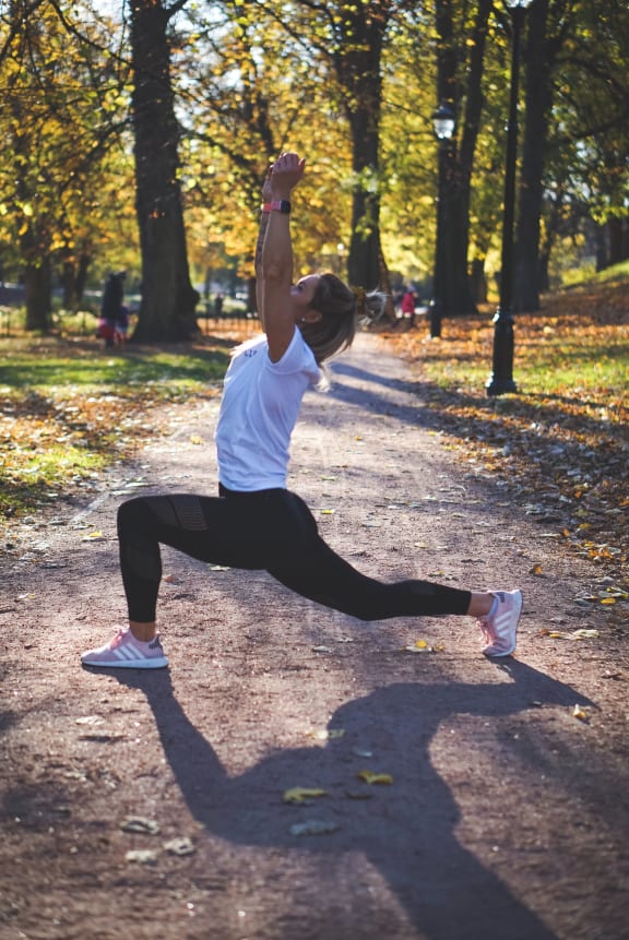 a woman in a white shirt and black leggings does a yoga pose in a park