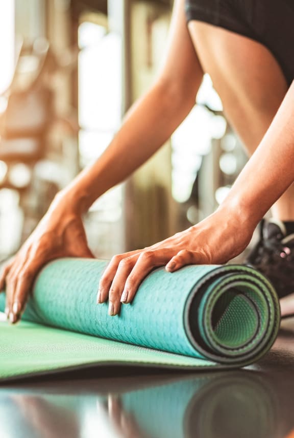 a woman rolling up a yoga mat in a gym