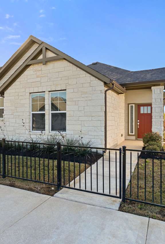 A beige house with a red door is surrounded by a black fence.