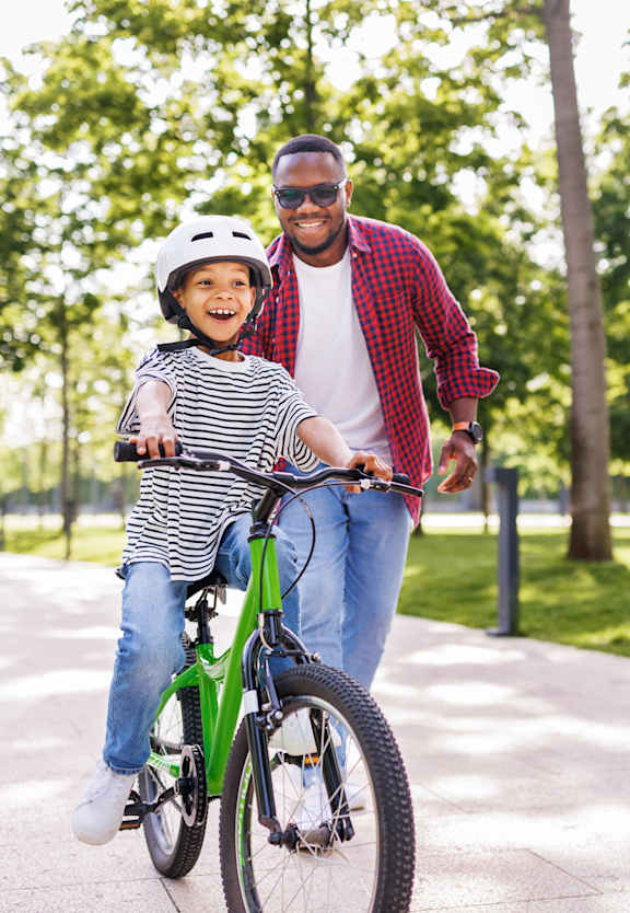 A man is teaching a child to ride a bike in a park.