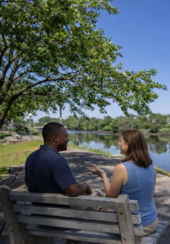 A man and a woman are sitting on a bench by a lake.