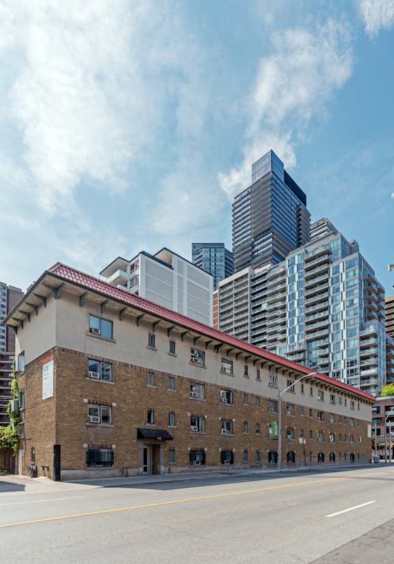 A large building with a red roof is in the foreground with a modern building in the background. at 608 Church Apartments, Toronto, ON, M4Y 2E7