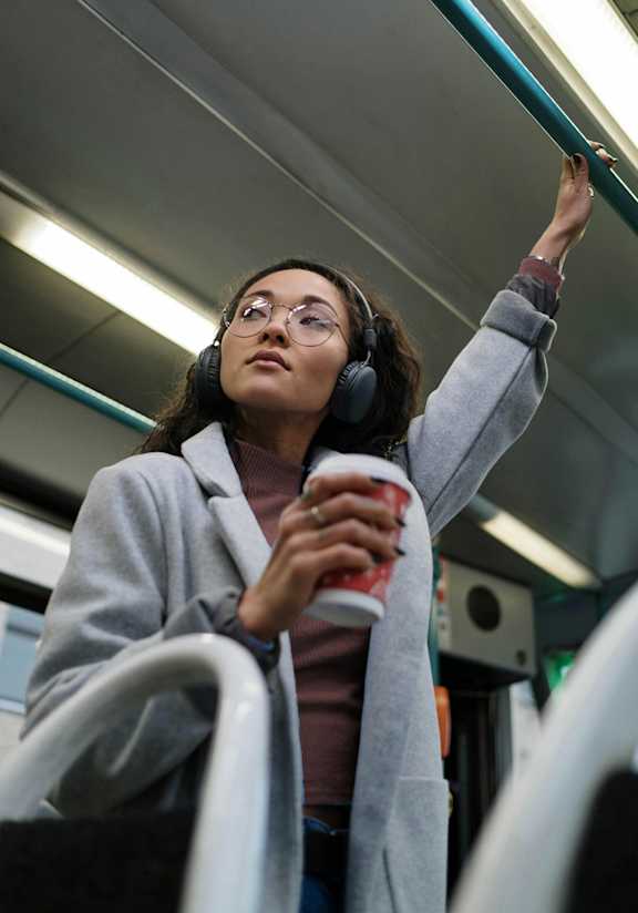 A woman in a grey coat is holding a red cup while standing in a subway car.