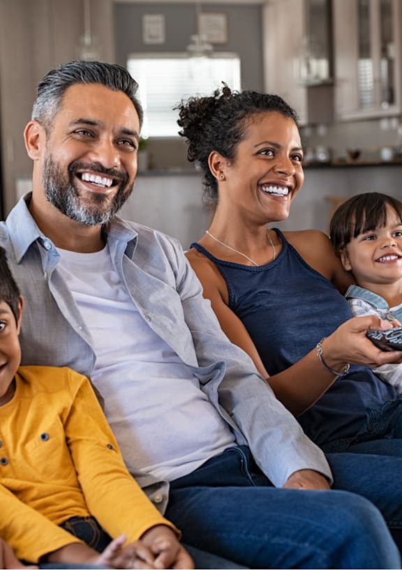 A family of four is sitting on a couch together.at Windrose Villas Apartments, Phoenix, AZ