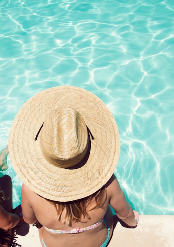 Two women wearing straw hats sitting by a pool.at Windrose Villas Apartments, Phoenix, 85029