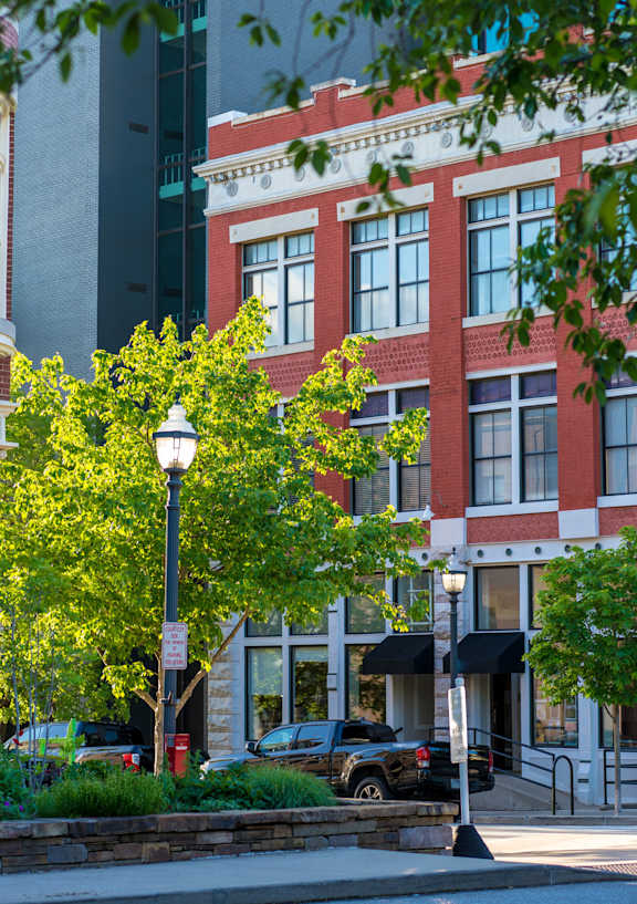 A street view of a building with a red brick facade and a green tree in front.