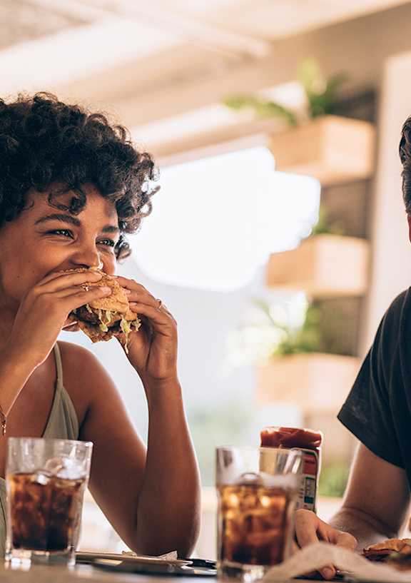 A man and a woman are eating burgers at a table.