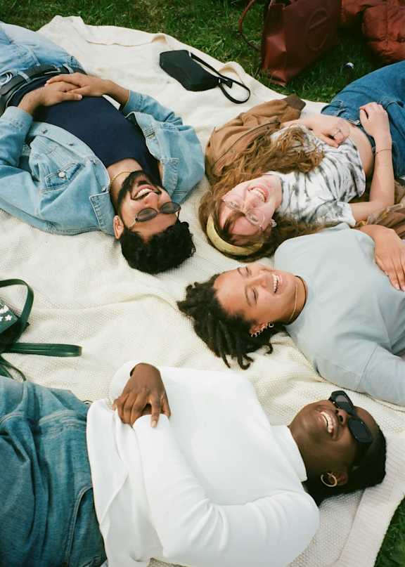 Four people lying on a blanket outdoors.