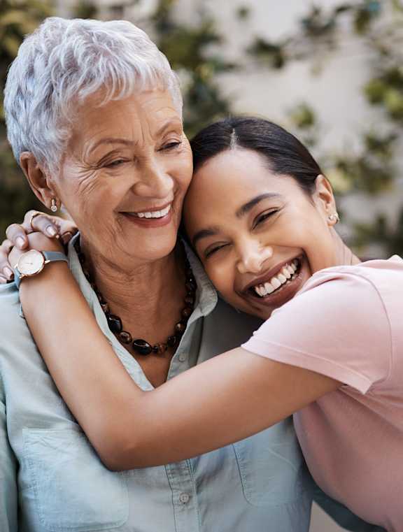 An older woman hugging a younger woman in a garden.