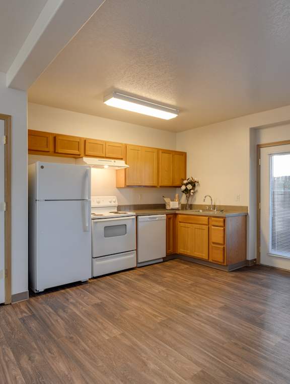 A kitchen with white appliances and wooden floors.