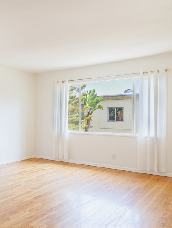 an empty room with white walls and a window and wood floors