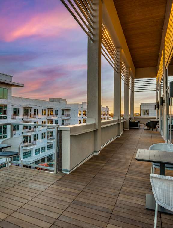 A balcony with chairs and tables overlooks a cityscape at dusk.