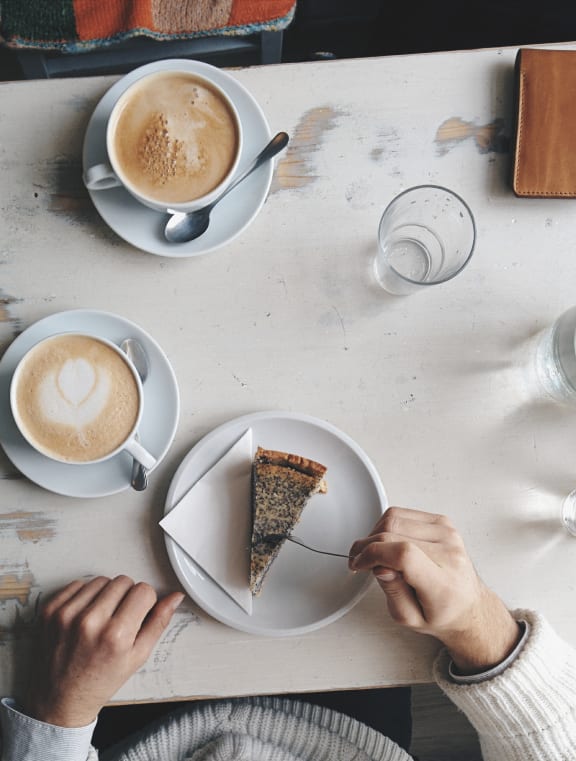 two people sitting at a table with coffee and a piece of cake