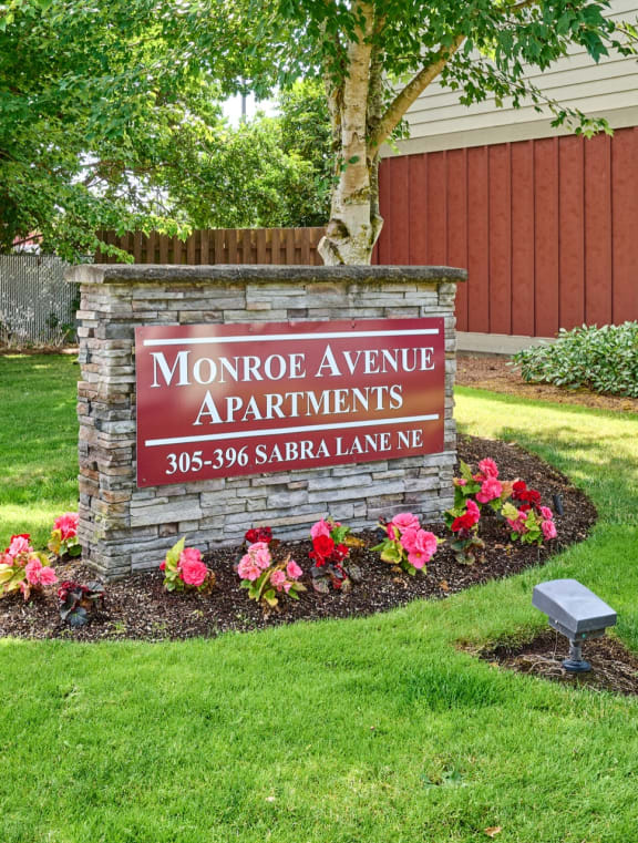 a sign for monroe avenue apartments in front of a lawn and flowers