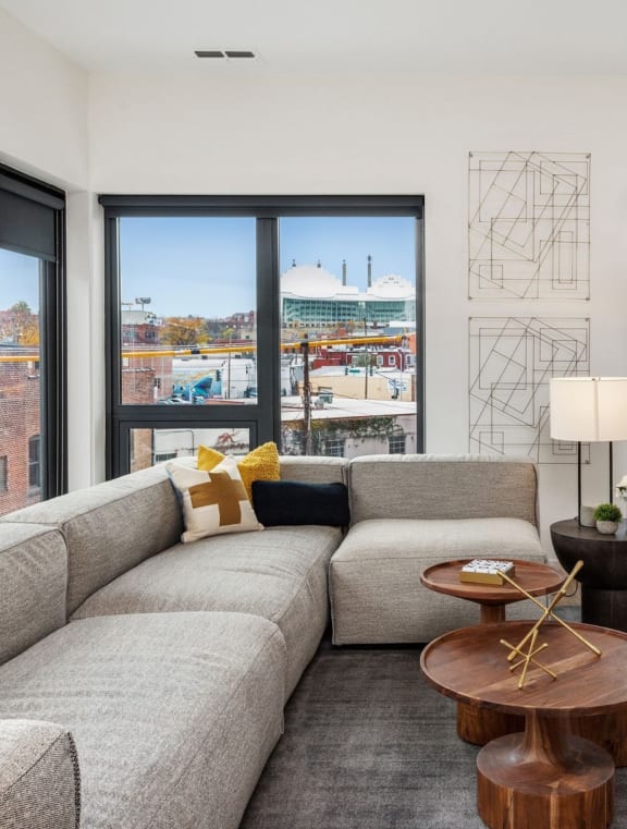 a living room with a gray couch and a large window with a view of a baseball field