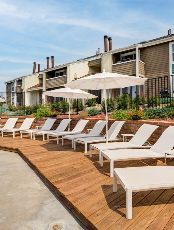 a row of white lounge chairs on a wooden deck in front of an apartment building