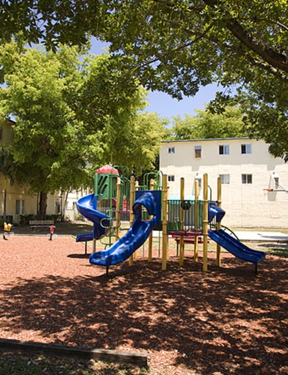 a playground in the middle of a grassy area with trees and a building in the background