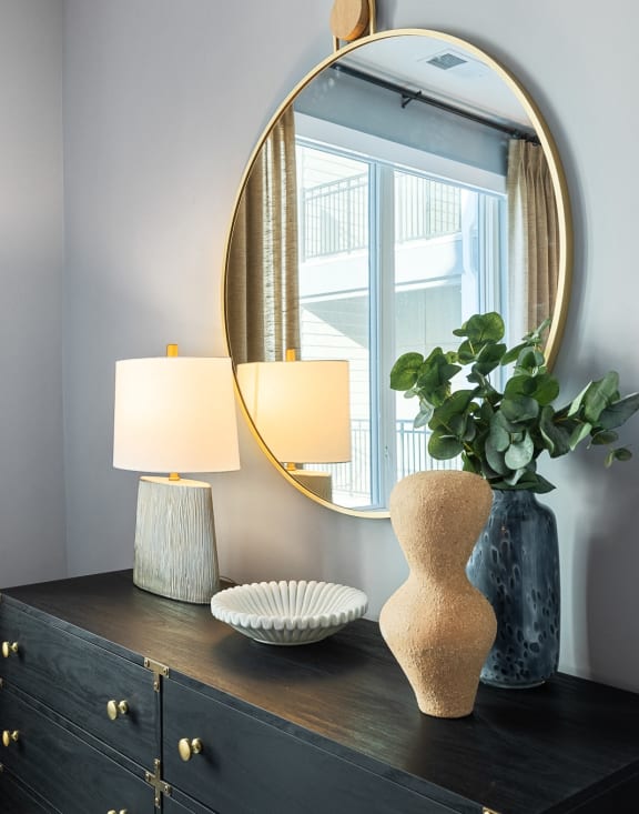 a dresser with a mirror and a vase with a plant and two lamps at Stonehill at West Orange, West Orange, New Jersey