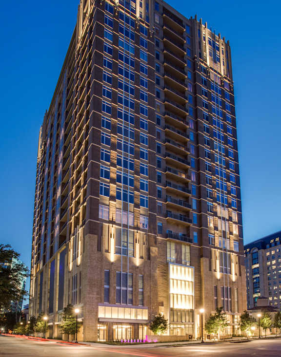 A tall building with many windows is lit up at night. at Uptown by Onni Apartments, Apartments, Dallas, TX