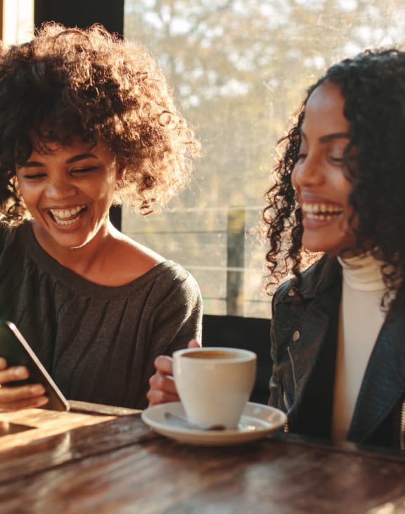 two women sitting at a table drinking coffee and looking at a cell phone