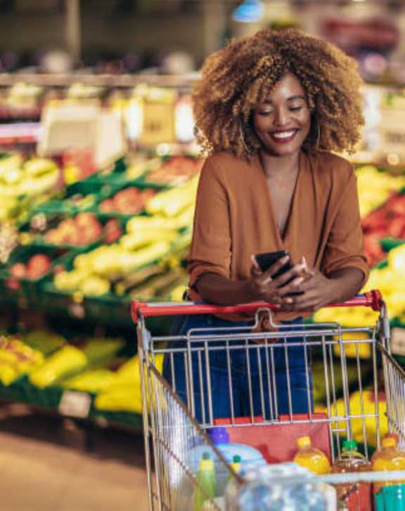 A woman is shopping in a grocery store with a cart full of items.