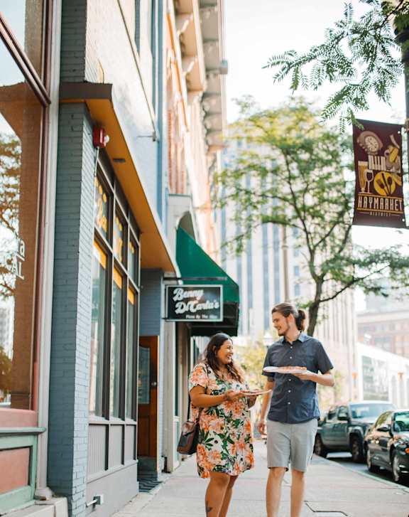 A man and woman walking down a sidewalk in front of a restaurant.