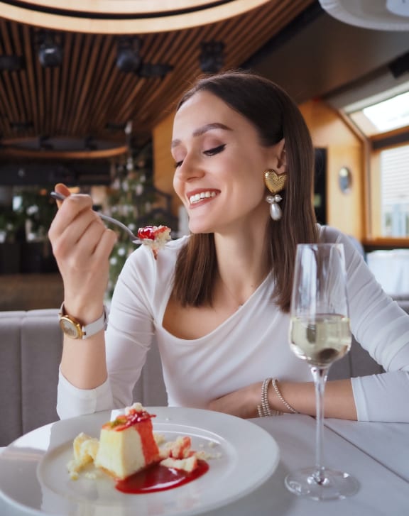portrait of a woman eating cake in a restaurant with a glass of wine