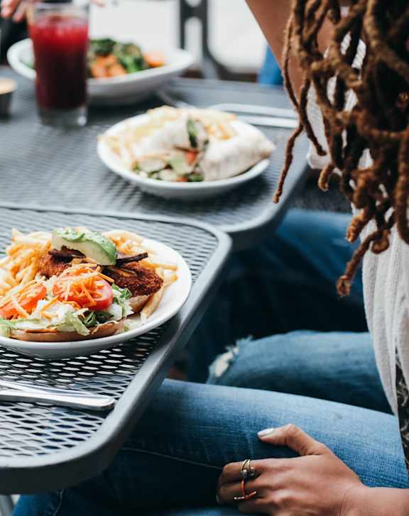 A woman with dreadlocks is sitting at a table with a plate of food in front of her.