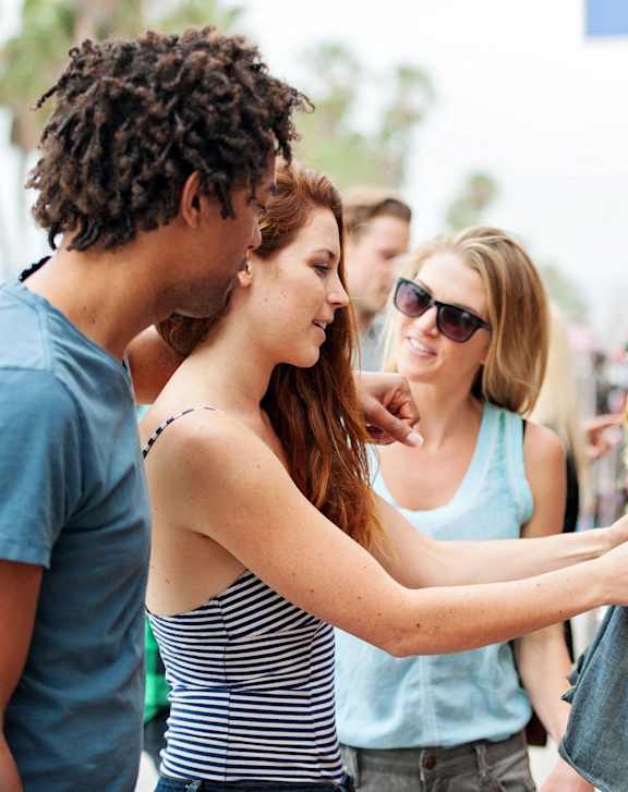 A woman is holding a denim jacket while standing next to a man and a woman in a clothing store.